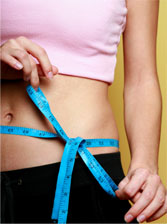 A woman is measuring her waist with a tape measure.